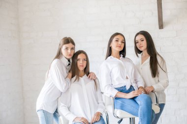 Pretty teenage girls models in trendy jeans and white shirts in the studio against the background of a white brick wall. Teenage fashion. beauty and fashion
