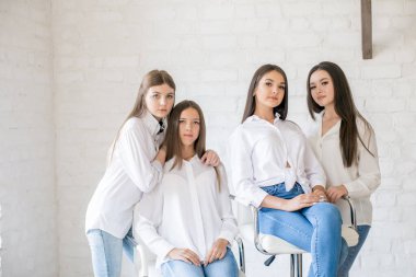Pretty teenage girls models in trendy jeans and white shirts in the studio against the background of a white brick wall. Teenage fashion. beauty and fashion