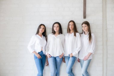 Pretty teenage girls models in trendy jeans and white shirts in the studio against the background of a white brick wall. Teenage fashion. beauty and fashion