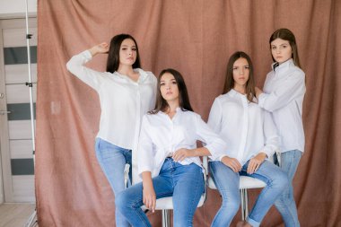 Stüdyoda modaya uygun kot ve beyaz gömlekli güzel genç kızlar var. Tekstil arka planında. Gençlik modası. güzellik ve moda