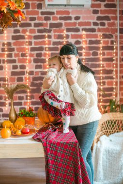 Beyaz örgü süveterler içinde, battaniye, yastık, balkabağı, sonbahar yaprakları ve elmalarla süslenmiş genç bir anne ve kız. Sonbahar havası. Cadılar Bayramı