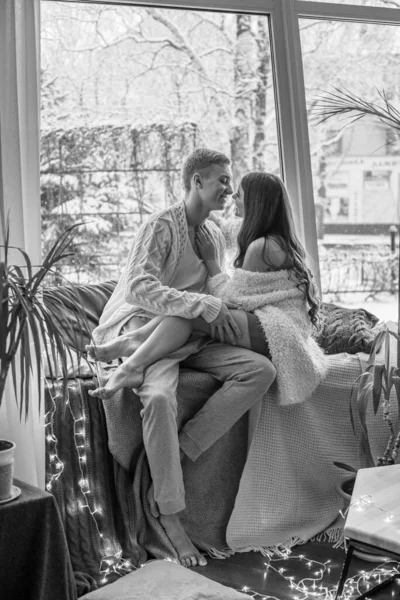 一对年轻貌美的夫妇 一男一女 在冬天的降雪时 穿着毛毯和温暖的毛衣坐在窗台上 拥抱着喝茶 感情和感觉 — 图库照片