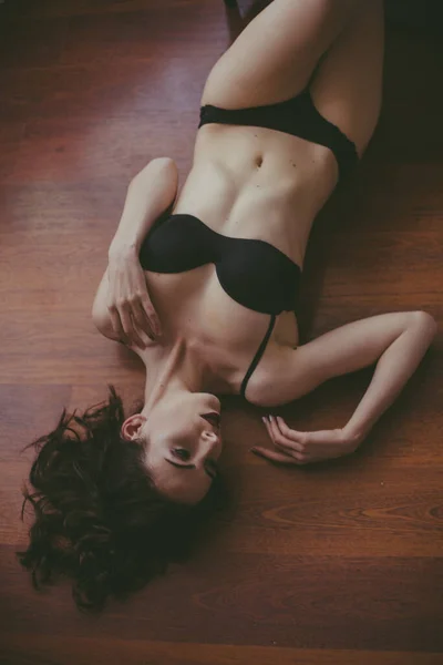 夜の化粧が施された黒いランジェリー姿の若い魅力的な女の子がベッドルームの床に横たわっています 美しさとファッション — ストック写真