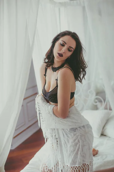 一个年轻迷人的女孩 深色头发 黑色内衣 晚上化妆 白色浴衣在卧室的白色床上 美与时尚 — 图库照片