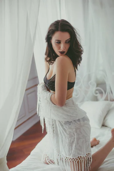 一个年轻迷人的女孩 深色头发 黑色内衣 晚上化妆 白色浴衣在卧室的白色床上 美与时尚 — 图库照片