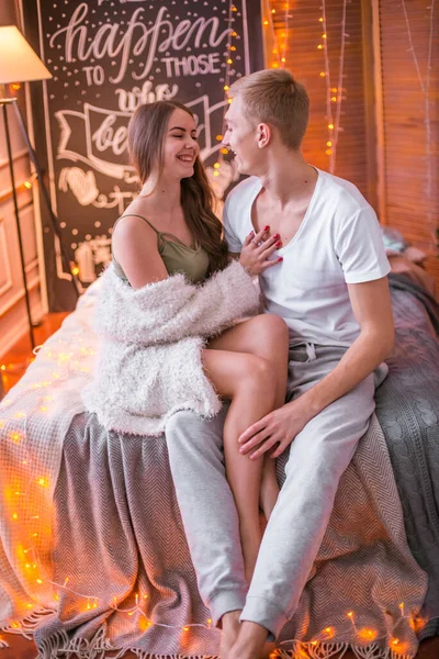 若く魅力的なカップル 男と女の子は ガーランドでクリスマスのために装飾された部屋のベッドに座って抱き合っています クリスマス気分 — ストック写真