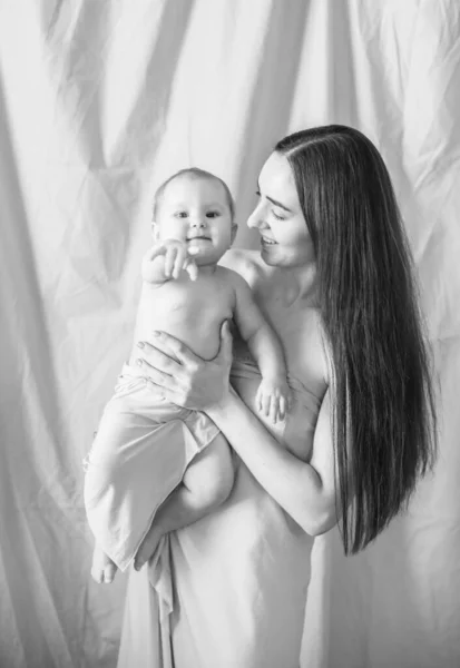年轻的母亲 有着一头长长的黑发 抱着一个可爱的小女孩 怀里抱着裸露的面料 背景是裸露的纺织品 快乐的母亲 — 图库照片