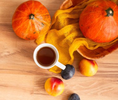 Bir fincan çay, balkabağı, erik, tekstil ve şeftaliden oluşan bir sonbahar dekoru ahşap arka planda.