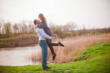 Bir çift uzun boylu genç adam ve uzun sarı saçlı kız arkadaşı nehir kıyısında şehrin dışında yürüyorlar. Duygular ve duygular. Yaşam tarzı. Ülke havası