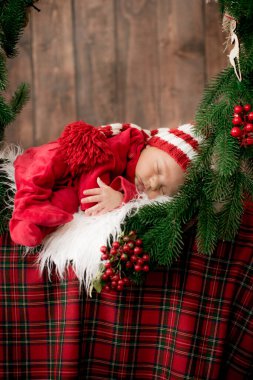 Kırmızı takım elbiseli ve şapkalı şirin bir bebek Noel süslemesinde uyuyor. Noel havası. Mutlu çocukluk.
