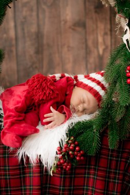Kırmızı takım elbiseli ve şapkalı şirin bir bebek Noel süslemesinde uyuyor. Noel havası. Mutlu çocukluk.