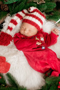 Kırmızı takım elbiseli ve şapkalı şirin bir bebek Noel süslemesinde uyuyor. Noel havası. Mutlu çocukluk.