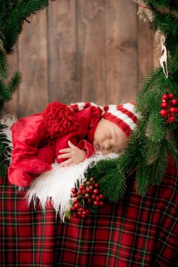 Kırmızı takım elbiseli ve şapkalı şirin bir bebek Noel süslemesinde uyuyor. Noel havası. Mutlu çocukluk.