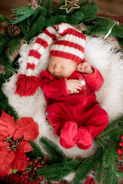 Kırmızı takım elbiseli ve şapkalı şirin bir bebek Noel süslemesinde uyuyor. Noel havası. Mutlu çocukluk.