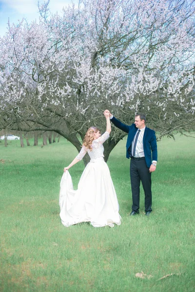 Gelin ve damat sarı uzun saçlı, bahar bahçesinde çiçek açan bir ağacın yanında beyaz elbiseli. Duygular ve duygular
