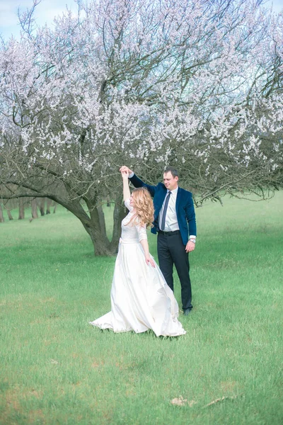 開花木の近くの春の庭の白いドレスにブロンドの長い髪の花嫁と新郎 感情や感情 — ストック写真