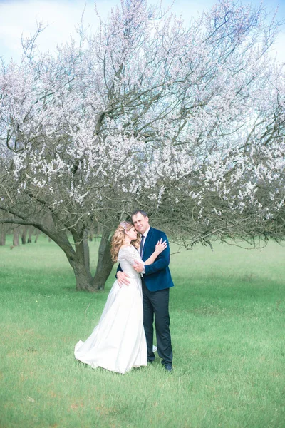 開花木の近くの春の庭の白いドレスにブロンドの長い髪の花嫁と新郎 感情や感情 — ストック写真