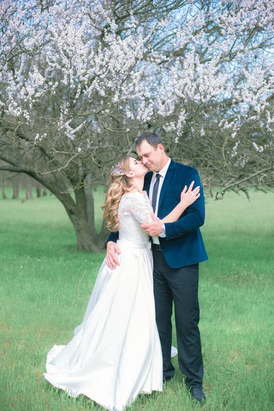 開花木の近くの春の庭の白いドレスにブロンドの長い髪の花嫁と新郎 感情や感情 — ストック写真