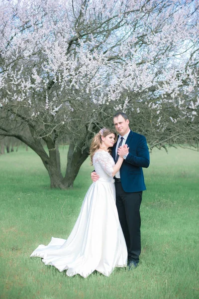 開花木の近くの春の庭の白いドレスにブロンドの長い髪の花嫁と新郎 感情や感情 — ストック写真