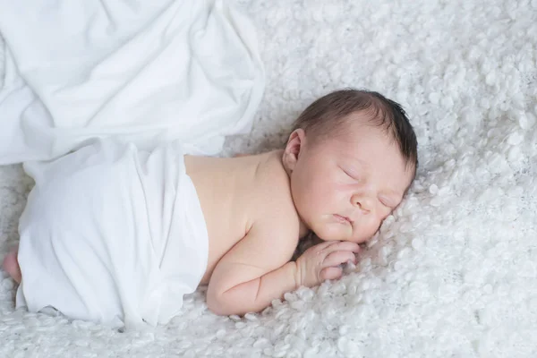 A cute little baby in a white blanket sleeps on a white boucl bedspread at home. Health and motherhood