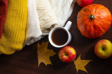 Bir fincan çay örülmüş sonbahar süveterleri masaya sıcak renkler, turuncu kabak sarısı akçaağaç yaprakları ve olgun kırmızı elmalarla birlikte. Sonbahar havası. Sonbahar ev konforu