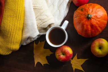 Bir fincan çay örülmüş sonbahar süveterleri masada sıcak renkler turuncu akçaağaç yaprakları ve olgun kırmızı elmalarla birlikte. Sonbahar havası. Sonbahar ev konforu