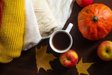 Bir fincan çay örülmüş sonbahar süveterleri masada sıcak renkler turuncu akçaağaç yaprakları ve olgun kırmızı elmalarla birlikte. Sonbahar havası. Sonbahar ev konforu