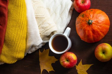 Bir fincan çay örülmüş sonbahar süveterleri masada sıcak renkler turuncu akçaağaç yaprakları ve olgun kırmızı elmalarla birlikte. Sonbahar havası. Sonbahar ev konforu