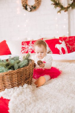 Bir yaşından küçük bir kız, havadar bir elbise içinde Noel için dekore edilmiş bir odada büyük bir yatakta çelenk ve çam iğnesi yastıklarının arasında. Noel havası. Çocuklar ve Noel