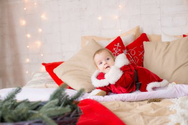 Noel için dekore edilmiş büyük bir odada Noel Baba kılığında küçük bir kız çocuğu çelenk ve çam iğneleri yastıklarının arasında. Noel havası. Çocuklar ve Noel
