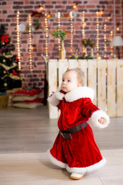 1歳未満の女の子は クリスマスのために装飾された部屋でサンタクロースの服を着て 贈り物 ガーランド 松葉の間のクリスマスツリーの近くにあります クリスマス気分 子供とクリスマス — ストック写真