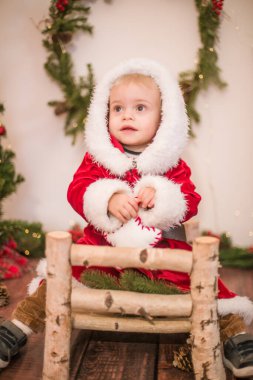 Noel için dekore edilmiş bir odada Noel Baba gibi giyinmiş şirin bir çocuk. Noel ve çocuklar