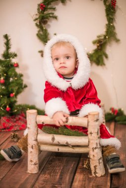 Noel için dekore edilmiş bir odada Noel Baba gibi giyinmiş şirin bir çocuk. Noel ve çocuklar