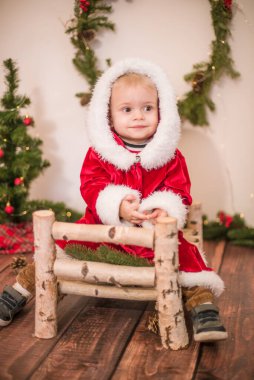 Noel için dekore edilmiş bir odada Noel Baba gibi giyinmiş şirin bir çocuk. Noel ve çocuklar
