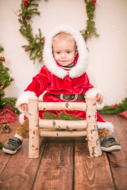 Noel için dekore edilmiş bir odada Noel Baba gibi giyinmiş şirin bir çocuk. Noel ve çocuklar