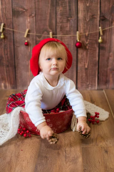 一个穿着红色格子花裙子 头戴红色贝雷帽的可爱小女孩 在装饰过圣诞节的房间里玩圆锥玩具和圣诞玩具 圣诞节和儿童 — 图库照片