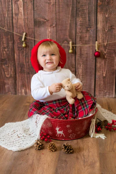 一个穿着红色格子花裙子 头戴红色贝雷帽的可爱小女孩 在装饰过圣诞节的房间里玩圆锥玩具和圣诞玩具 圣诞节和儿童 — 图库照片