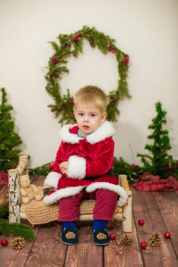 Noel için dekore edilmiş bir odada Noel Baba gibi giyinmiş şirin bir çocuk. Noel ve çocuklar