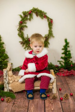 Noel için dekore edilmiş bir odada Noel Baba gibi giyinmiş şirin bir çocuk. Noel ve çocuklar