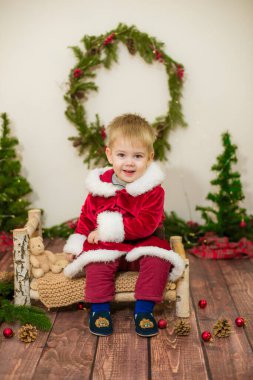 Noel için dekore edilmiş bir odada Noel Baba gibi giyinmiş şirin bir çocuk. Noel ve çocuklar