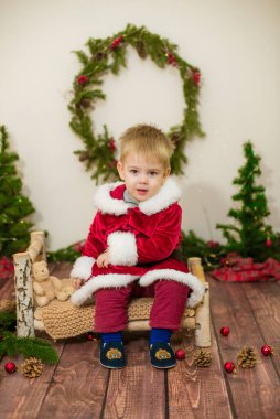 Noel için dekore edilmiş bir odada Noel Baba gibi giyinmiş şirin bir çocuk. Noel ve çocuklar