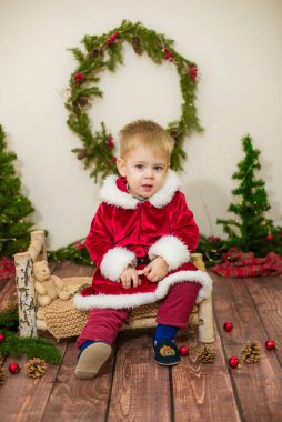Noel için dekore edilmiş bir odada Noel Baba gibi giyinmiş şirin bir çocuk. Noel ve çocuklar