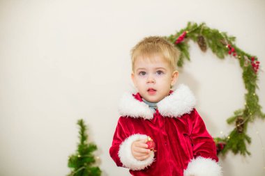 Noel için dekore edilmiş bir odada Noel Baba gibi giyinmiş şirin bir çocuk. Noel ve çocuklar