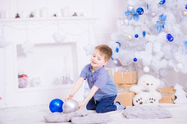 Noel için dekore edilmiş bir odada, beyaz bir Noel ağacının yanında mavi gömlekli yakışıklı bir çocuk. Aile Noel 'i Noel havası