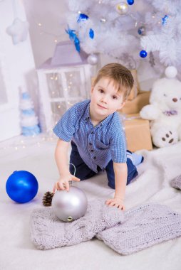 Noel için dekore edilmiş bir odada, beyaz bir Noel ağacının yanında mavi gömlekli yakışıklı bir çocuk. Aile Noel 'i Noel havası