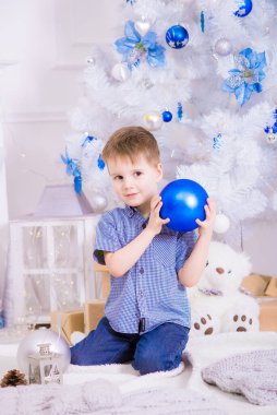 Noel için dekore edilmiş bir odada, beyaz bir Noel ağacının yanında mavi gömlekli yakışıklı bir çocuk. Aile Noel 'i Noel havası
