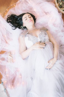 Noel için çam iğneleri ve ışıl ışıl çelenklerle süslenmiş bir odada koyu renk saçlı hamile bir kadın. Noel havası. Hamilelik