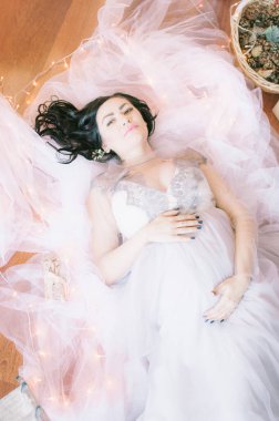 Noel için çam iğneleri ve ışıl ışıl çelenklerle süslenmiş bir odada koyu renk saçlı hamile bir kadın. Noel havası. Hamilelik