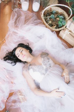 Noel için çam iğneleri ve ışıl ışıl çelenklerle süslenmiş bir odada koyu renk saçlı hamile bir kadın. Noel havası. Hamilelik