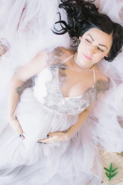 Young pregnant woman with dark hair in airy dress in a room decorated with pine needles and sparkling garlands for Christmas. Christmas mood . Pregnancy